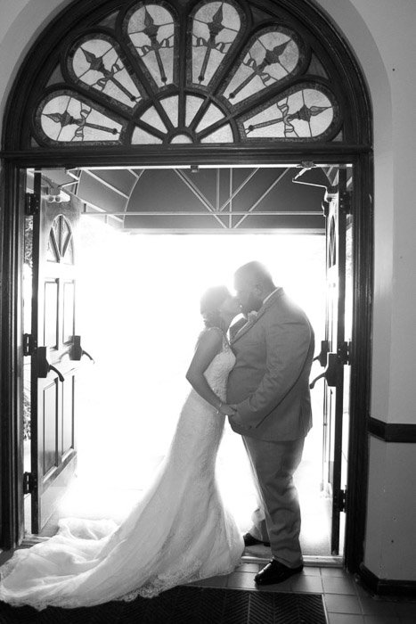 A black and white photo of the newlywed couple kissing under an arched doorway - wedding photography lighting tips