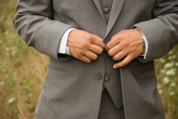 Wedding photography close up of a man buttoning his suit. 