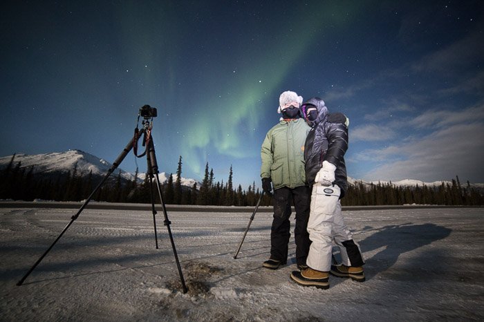 两位摄影师拿着相机和三脚架拍摄北极光的照片。冬季摄影。