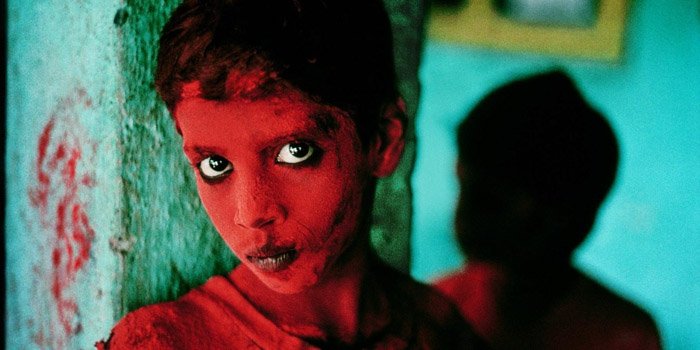 Steve McCurry portrait of a child painted with red face paint against a green wall - famous photographers work 