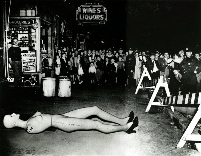 Weegee photo of a crowd of people looking at a crime scene, with a shop mannequin placed on the ground 