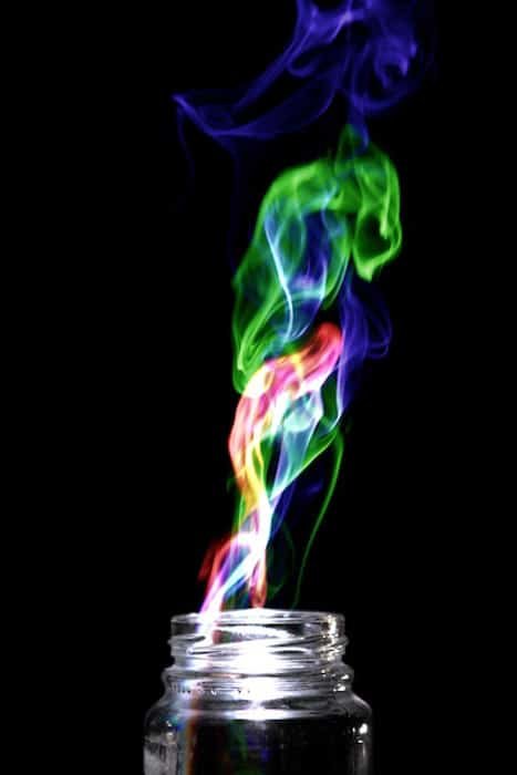 黑色背景下，从玻璃罐中冒出五颜六色的烟雾。通过“哈里斯效应”创意摄影项目实现。