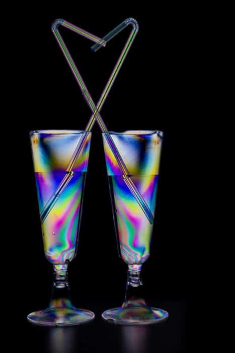 两个鸡尾酒杯装满了在黑色背景下的彩色光弹性效果