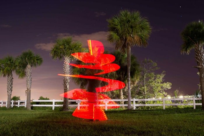A palm tree at night, with red spiral light painting wrapped around it 