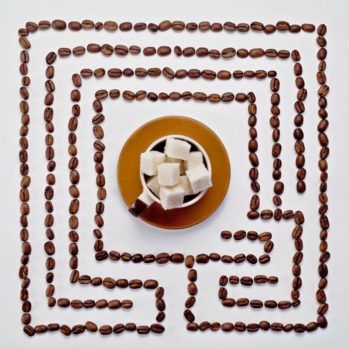 Overhead shot of a maze of coffee beans with a cup of sugar cubes in the centre