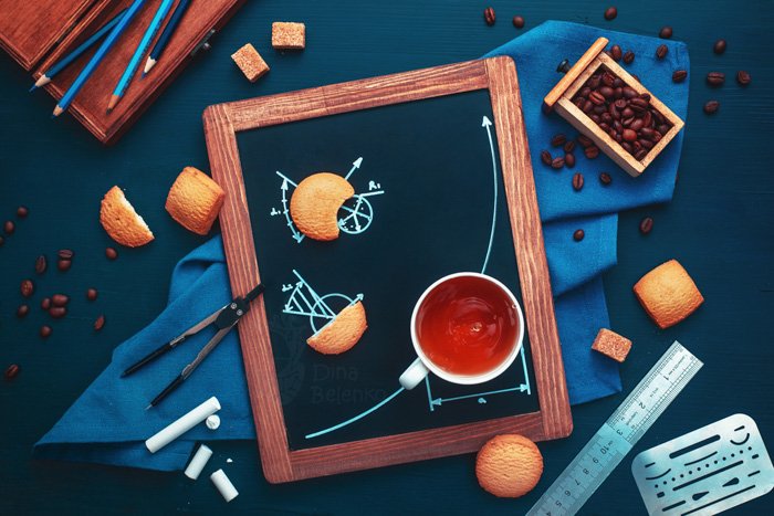 Overhead still life using coffee cups, biscuits, chalkboard, pencils and coffee beans to tell a story about a high school kid doing their geometry homework