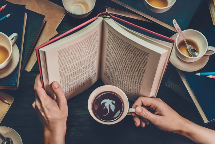 Conceptual still life shot of a person reading a fantasy book and seeing a dragon in a coffee-cup reflection.