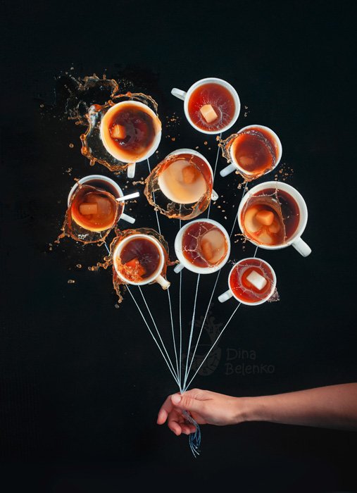 A playful food photography shot of a person holding strings to nine coffee cups as if they were holding a bunch of balloons