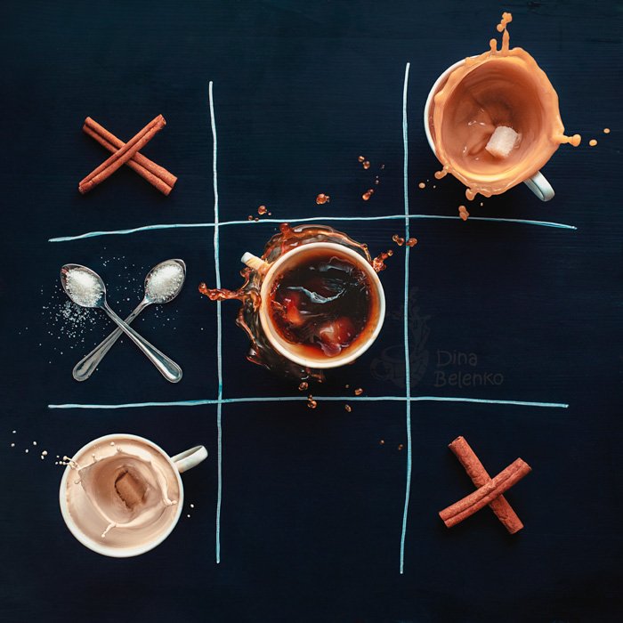 An overhead creative coffee photto of the game tic tac toe created with coffee cups, cinnamon sticks and spoons