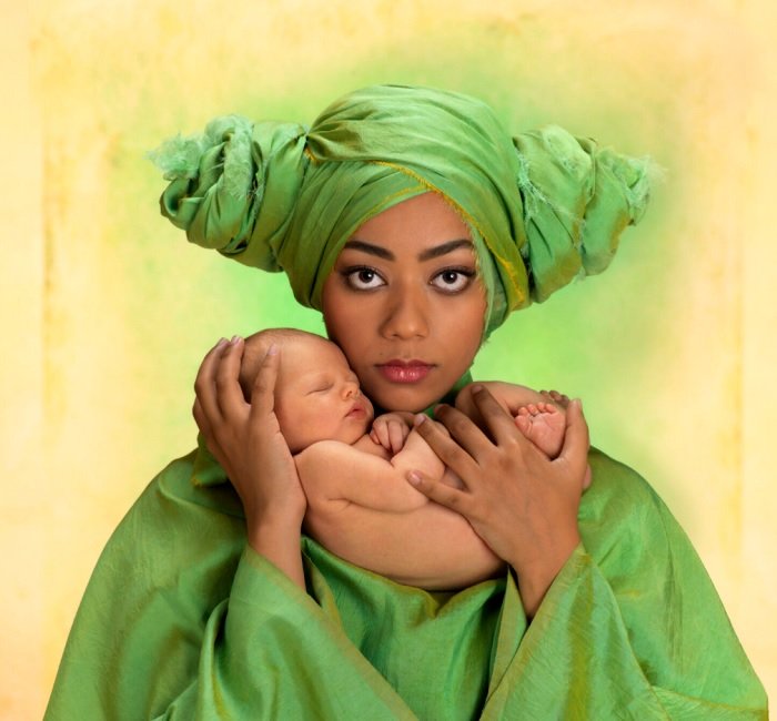 Woman in green robe and turban holding a newborn baby