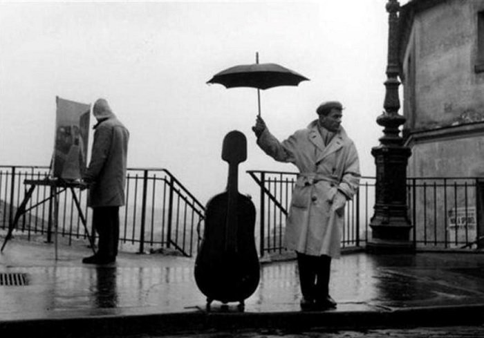 Man holding an umbrella above a cello case