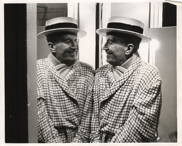 Man in dressing gown and hat looking into a mirror