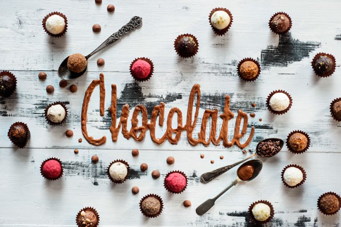 The word chocolate made from food typography glazing with chocolates, candies and tea spoons on a white wooden background. 