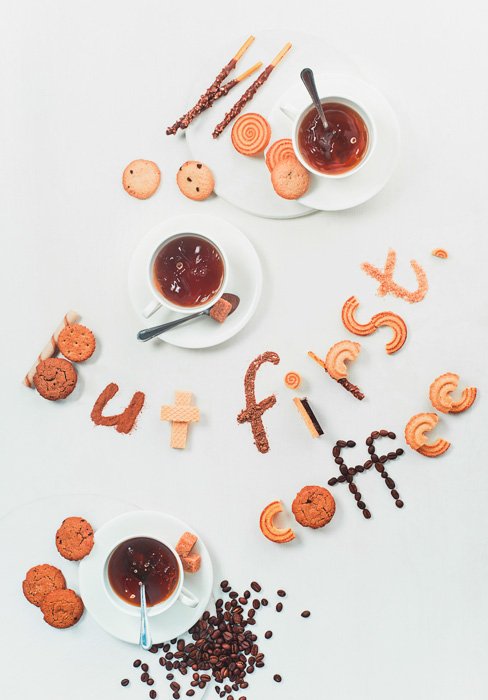 An overhead food art shot featuring coffee cups, saucers, biscuits and coffee beans with food typography