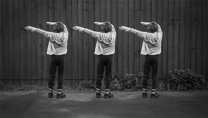 A black and white multiplicity photography example of three of the same little girl dancing outdoors