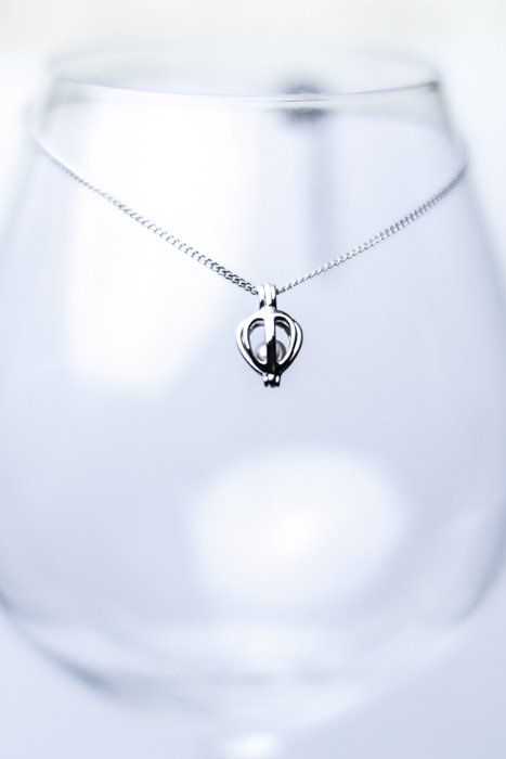 A product image close up of a necklace displayed on a wine glass