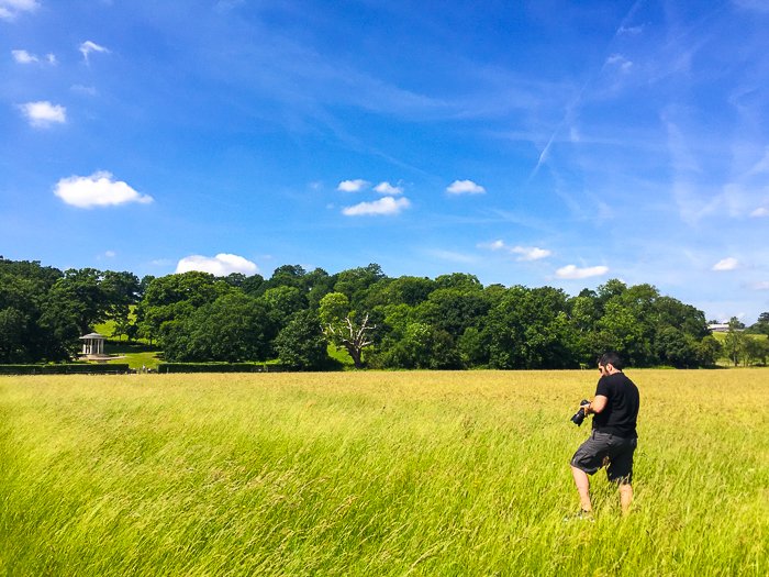 A photographer checking his camera settings in a grassy landscape on a clear day with blue skies