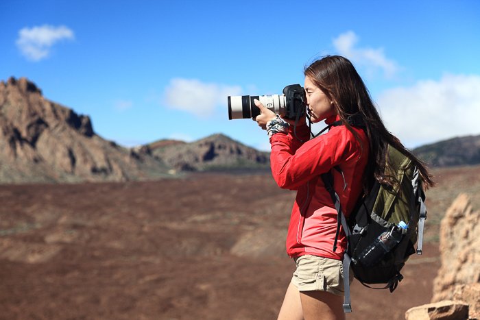 A female photographer adjusting her camera settings in a rocky landscape with blue skies