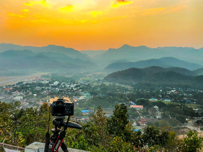 A Canon DSLR camera on a tripod, pointed at a beautiful landscape at sunset