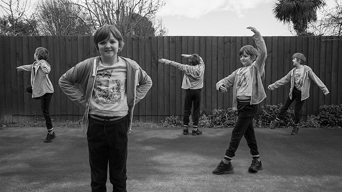 A black and white, wide angle multiplicity photography example of five of the same little girl dancing outdoors