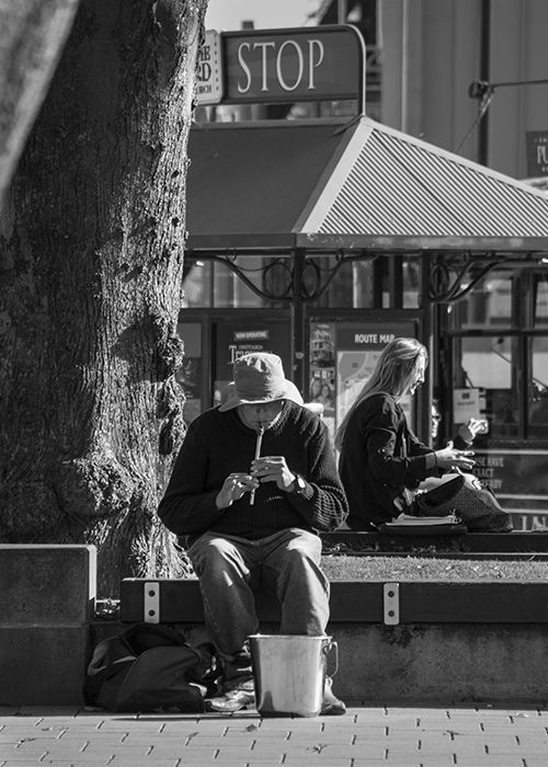 Black and white street portrait of a man playing a flute outdoors on a bright sunny day