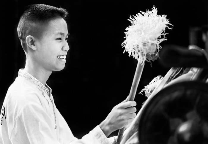 Portrait of a teenage boy playing a large drum during the annual flower parade in Chaing Mai, Thailand. Black background photography.