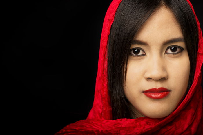 An Asian woman with red scarf poses for portrait against a dark background - how to create a black background for photography portraits.