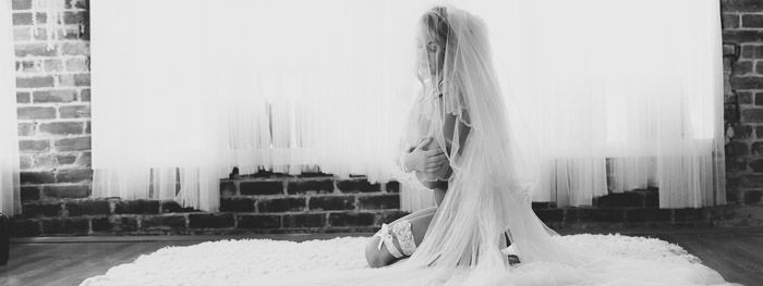 Ethereal black and white boudoir photography shot of a girl in bridal wear sitting on a rug