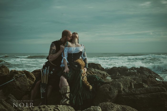 Romantic boudoir photography shot of a couple sitting on rocks with the sea behind