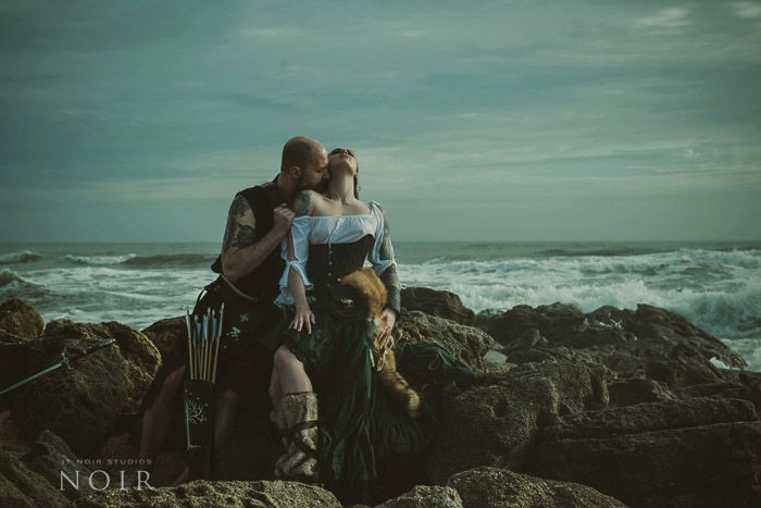 Romantic boudoir photography shot of a couple sitting on rocks with the sea behind