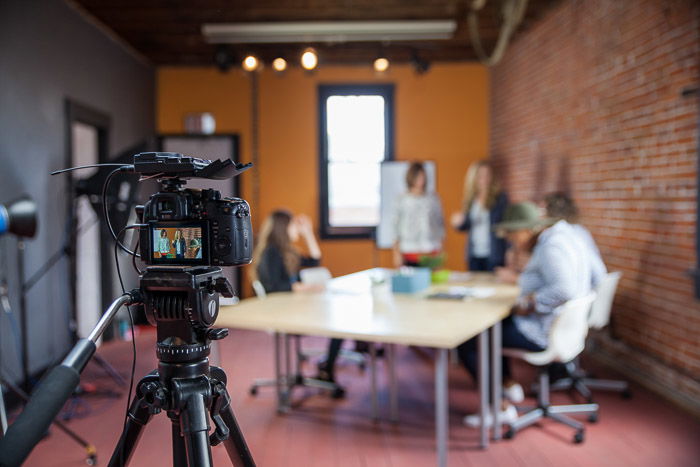 A commercial photography shoot set up with a dslr camera on tripod in the foreground, blurred background of people around a table