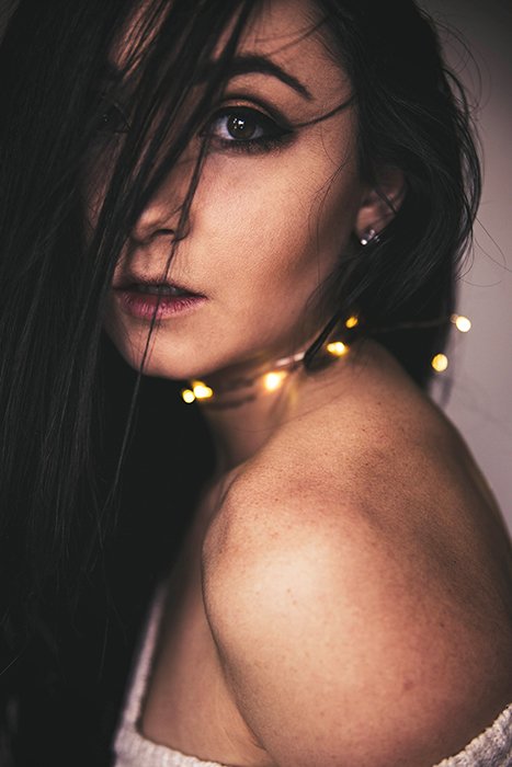 Atmosphere portrait of a dark haired female posing with fairy lights around her neck