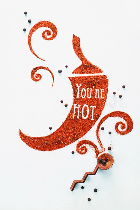 A food art shot with the words 'you're hot' created with spices in the shape of a paprika on white background