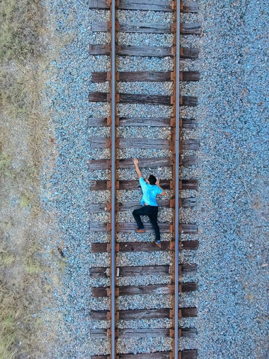 A photo of a man on train tracks, taken from overhead to give the illusion that he is climbing upwards