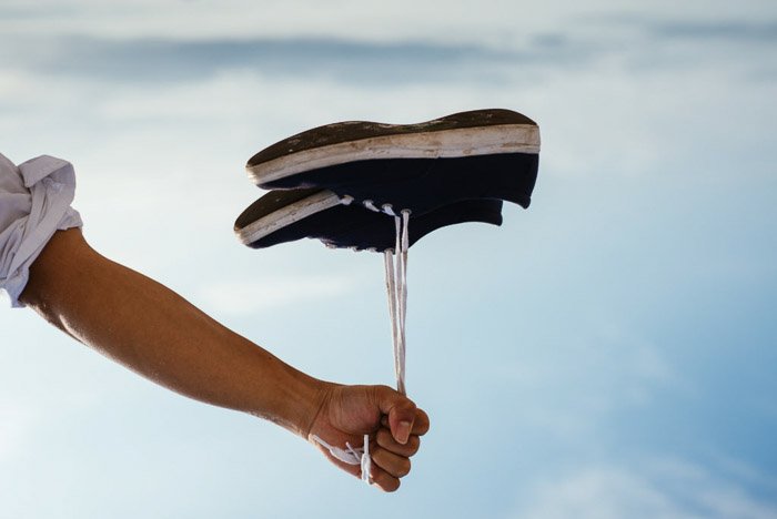 A person holding a pair of shoes by the laces which look like they are floating like a balloon