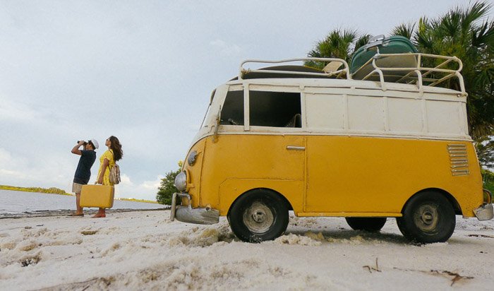 A couple on a beach with a yellow van behind them 