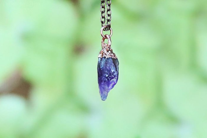 A close up of an amethyst necklace on blurry green background