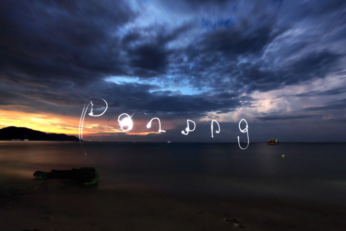 Words drawn in the sky over a seascape at night, using a smartphone's flashlight for light painting photography