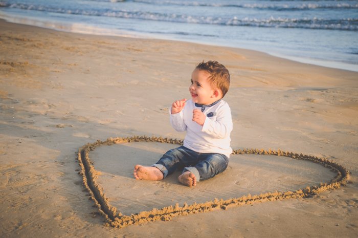 A young boy sits in the middle of a love heart drawn in the sand, creative beach photography ideas.