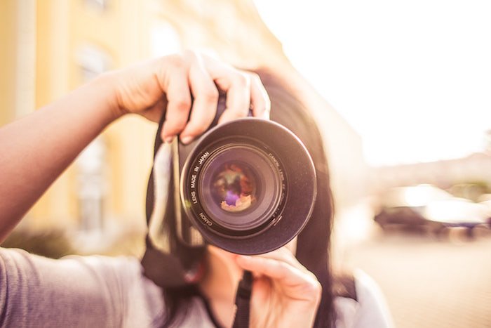 A girl pointing a camera towards the photographer on soft blurry background - photography and camera insurance tips