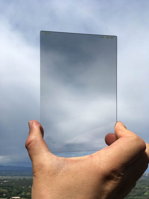 A person holding a lens filter against the sky 