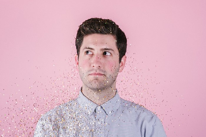 Portrait of a man covered in falling glitter posing in front of a pink photography background