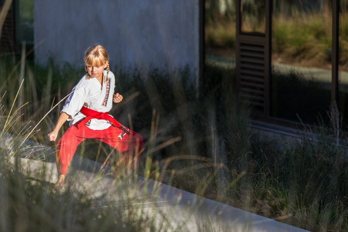 A portrait of a little girl in a karate pose outdoors