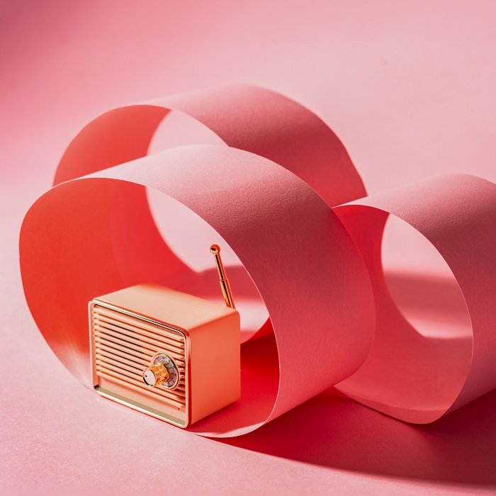 Un ejemplo de estilo de fotografía de producto de una radio vintage rodeada de papel rosa sobre fondo rosa