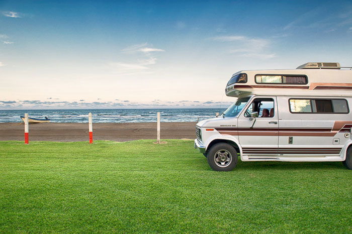 A camper van parked on grass with seascape behind 