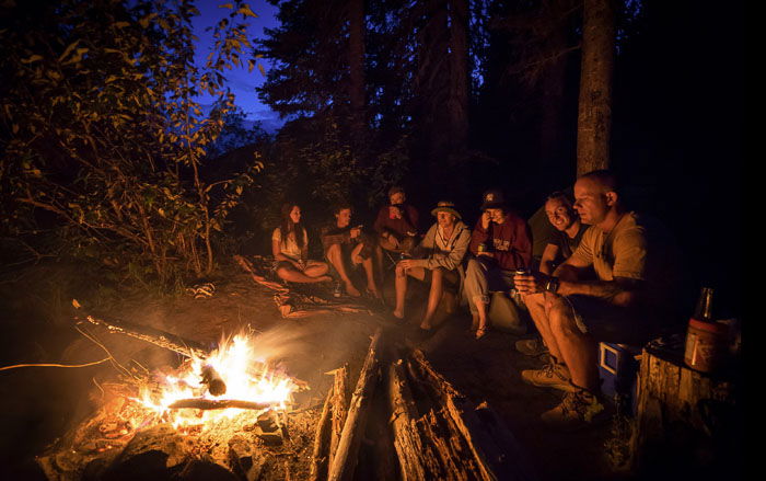 A group of people sitting around a campfire in a forest at night