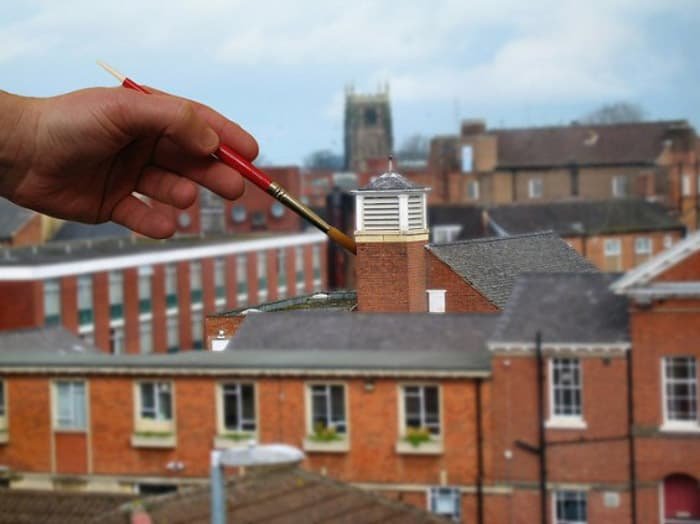  Cool tilt shift photography image where the photographer holds a paintbrush into the scene from the camera, making it look the same size as the buildings.