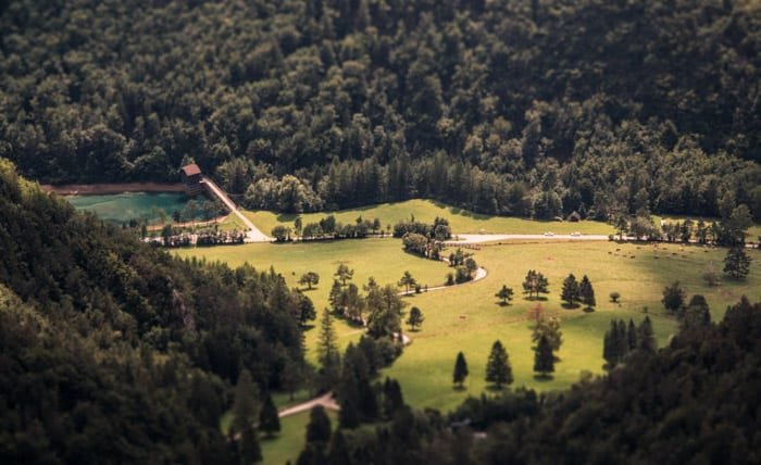 A beautiful countryside area surrounded by trees. The use of tilt-shift photography makes the scene look like its a model.