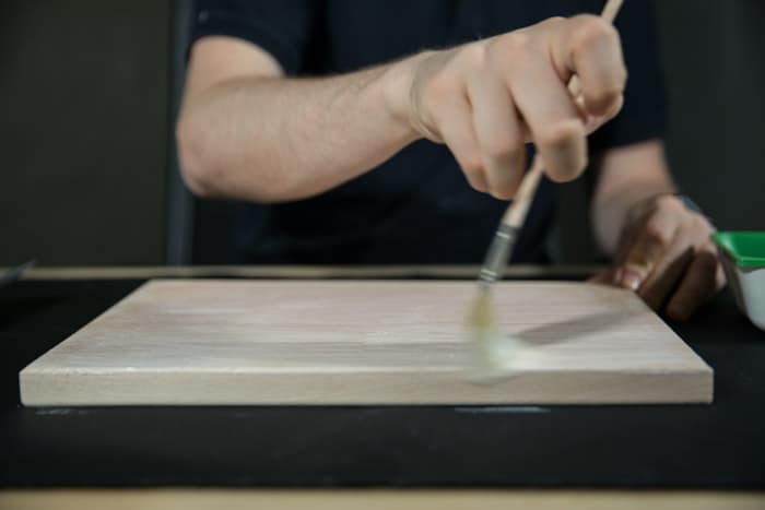 A man painting a wooden board with glue for photo transfer to wood