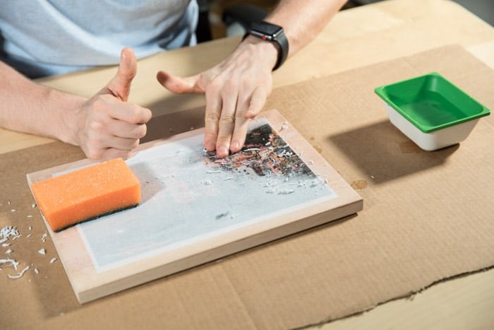 A man rubbing a wooden board to transfer photos to wood